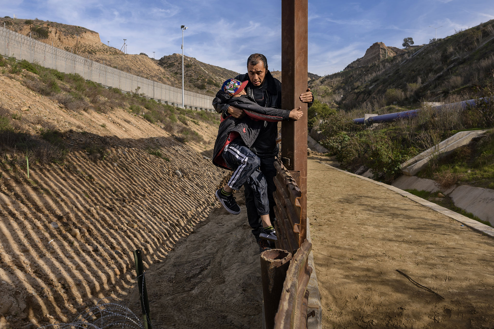 Un hombre sostiene en brazos a su hijo mientras escalan la valla fronteriza de los los EE. UU. antes de saltar desde Tijuana, México, el 22 de diciembre de 2018.