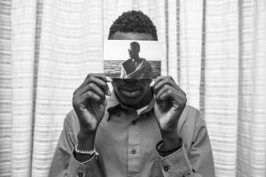 Malick posa para un retrato dentro de su habitación del Hotel Colibri, sosteniendo una foto suya tomada el 2 de agosto de 2016, minutos después de ser rescatado de las aguas del Mediterráneo. Sobrevivió después de siete horas de viaje desde la salida de la costa de Libia, viajando en un bote de goma con 120 personas a bordo.