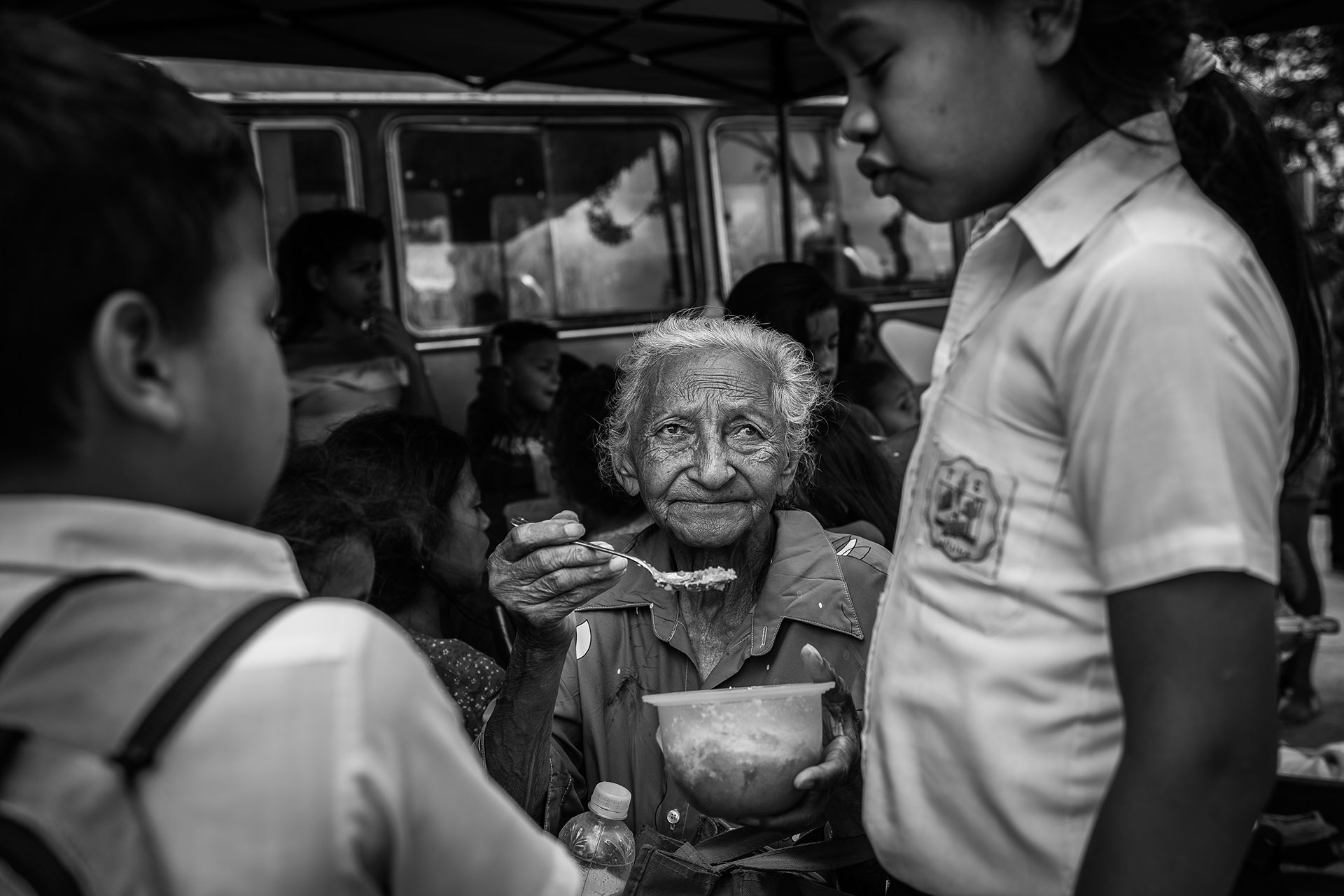 An elderly lady gives food to a child in a social canteen organized by a local NGO. According to Caritas, 65% of the youth they work with suffers from malnutrition.