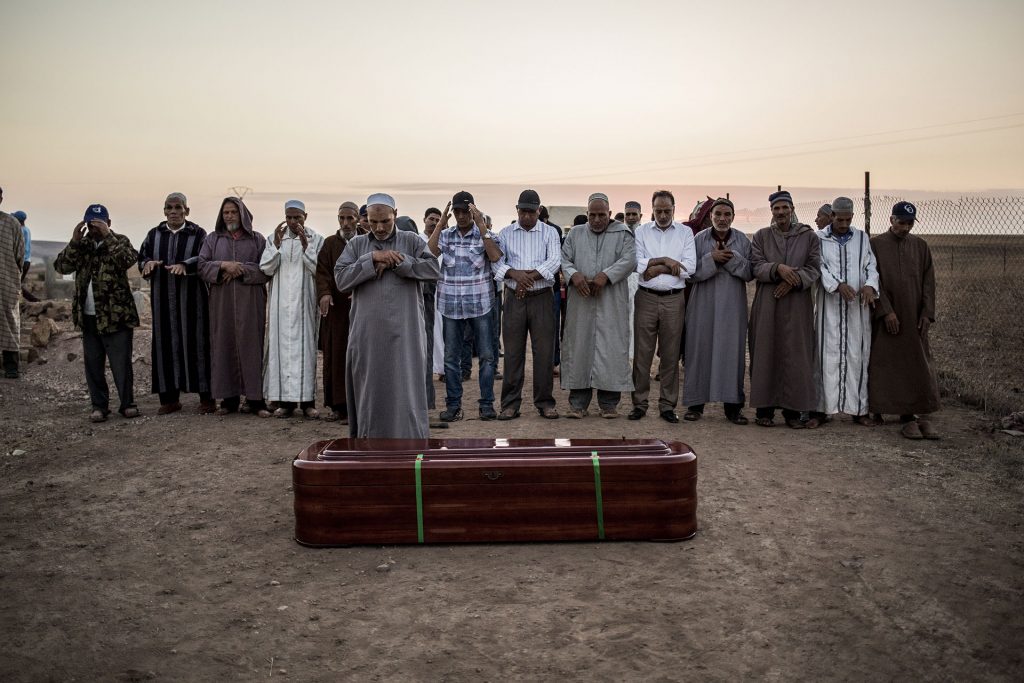 Men stand praying moments before Zohra Sarrouj’s burial.