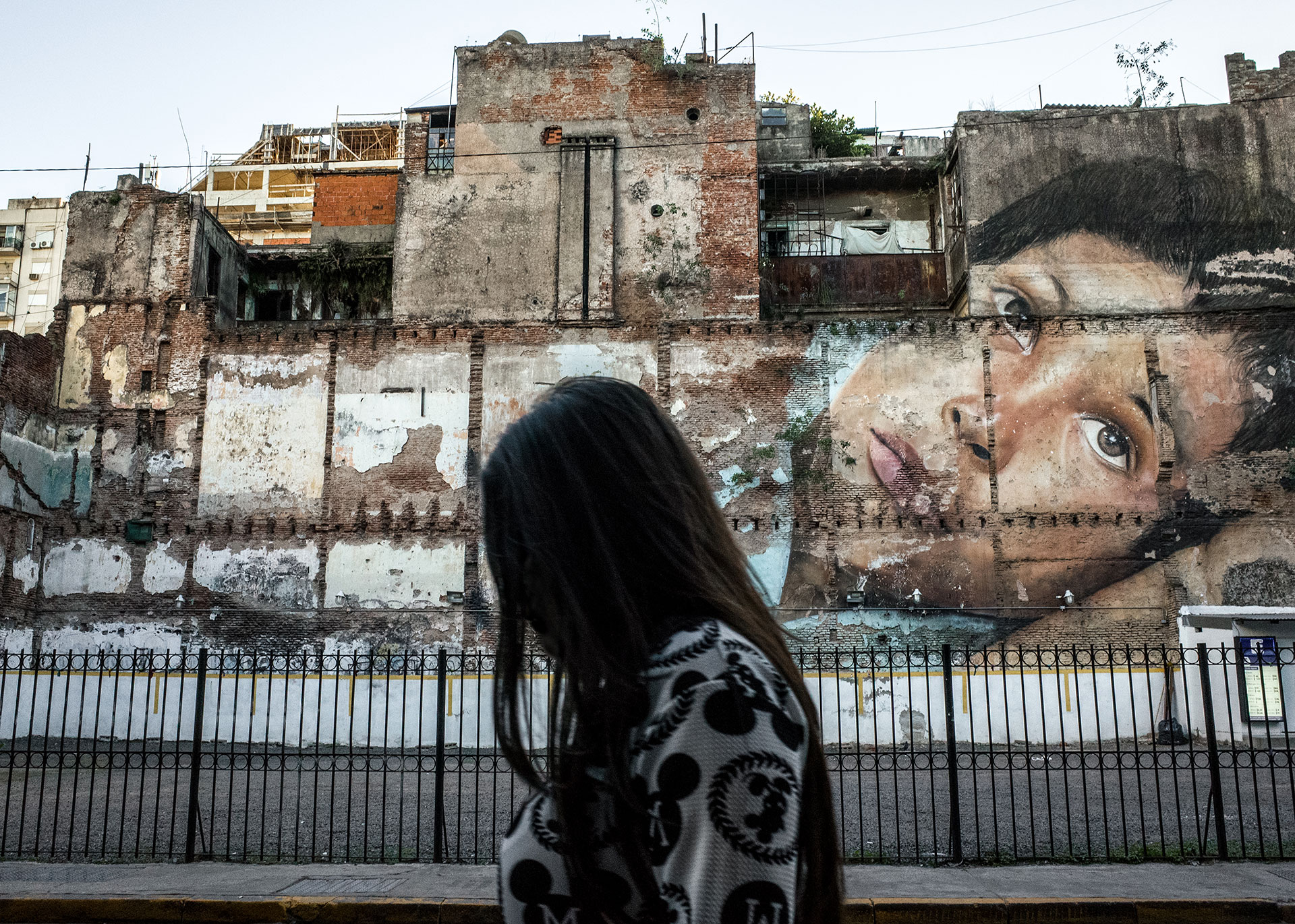 Buenos Aires. A woman is walking in one street of the center with a huge mural in the background. All the city is full of wall painted, sometimes entire buildings or streets. Often these paintings are political, many are against gender violence, injustice and people who disappeared.