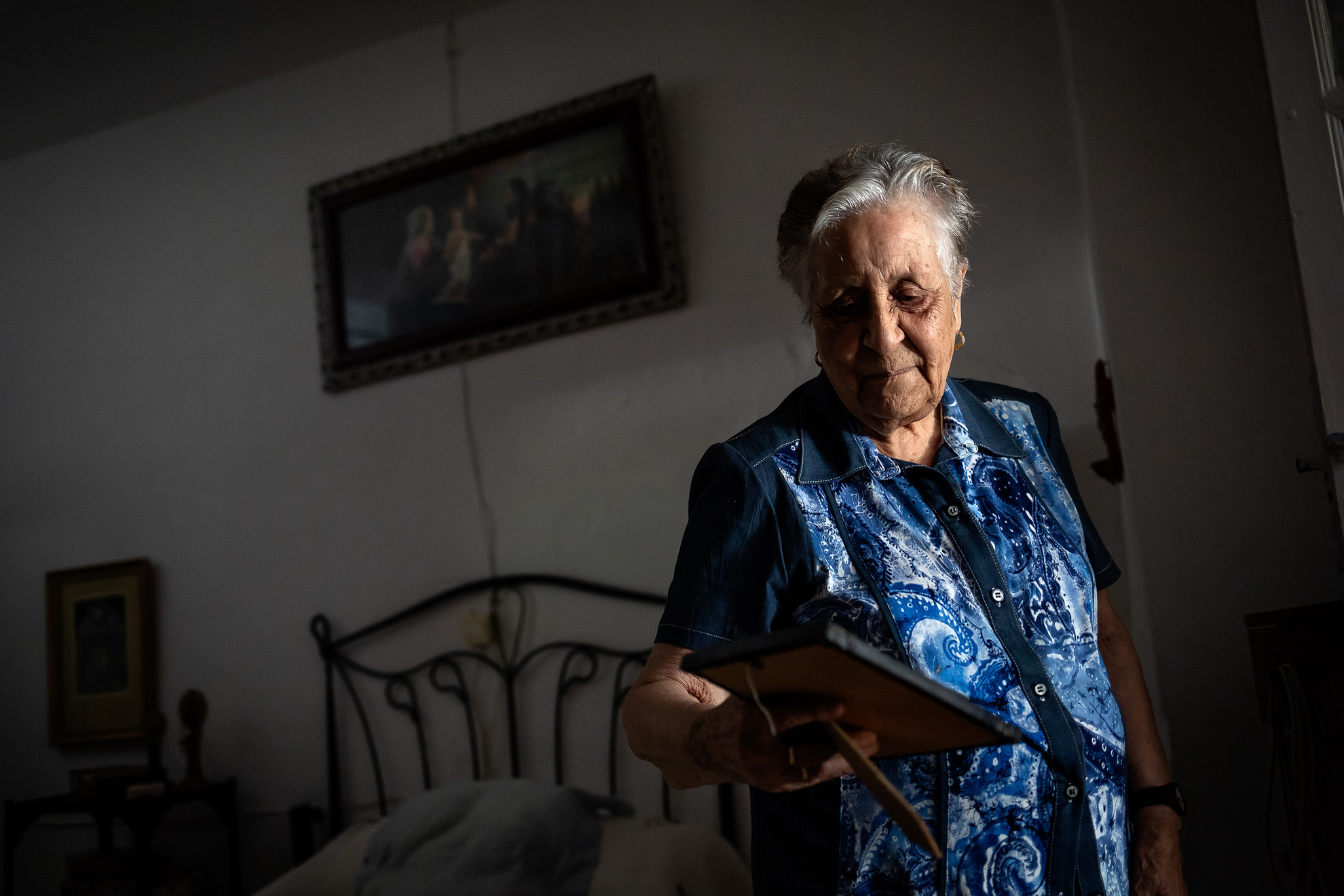 Although everyone knows her as Pilar, legally her name is Mª Dolores. The story behind says that when Pilar was born, her mother, Mª Dolores, sent her father to register her newborn granddaughter. And when he arrived at the registry, the grandfather forgot the name that they told him to give the little girl, and then he deduced, wrongly, that the name would be the same as his daughter, Mª Dolores. The error was discovered 6 years later when they went to baptize the girl and discovered that Pilar was actually Mª Dolores. But she remains for everyone as Pilar, the same one who has finally been able to return to her home in Aracena, after spending all the confinement by COVID-19 at her niece's house. When she returns home after two months, she stares at the portrait of her mother, Mª Dolores, to whom she owes the name, although she is called Pilar.
