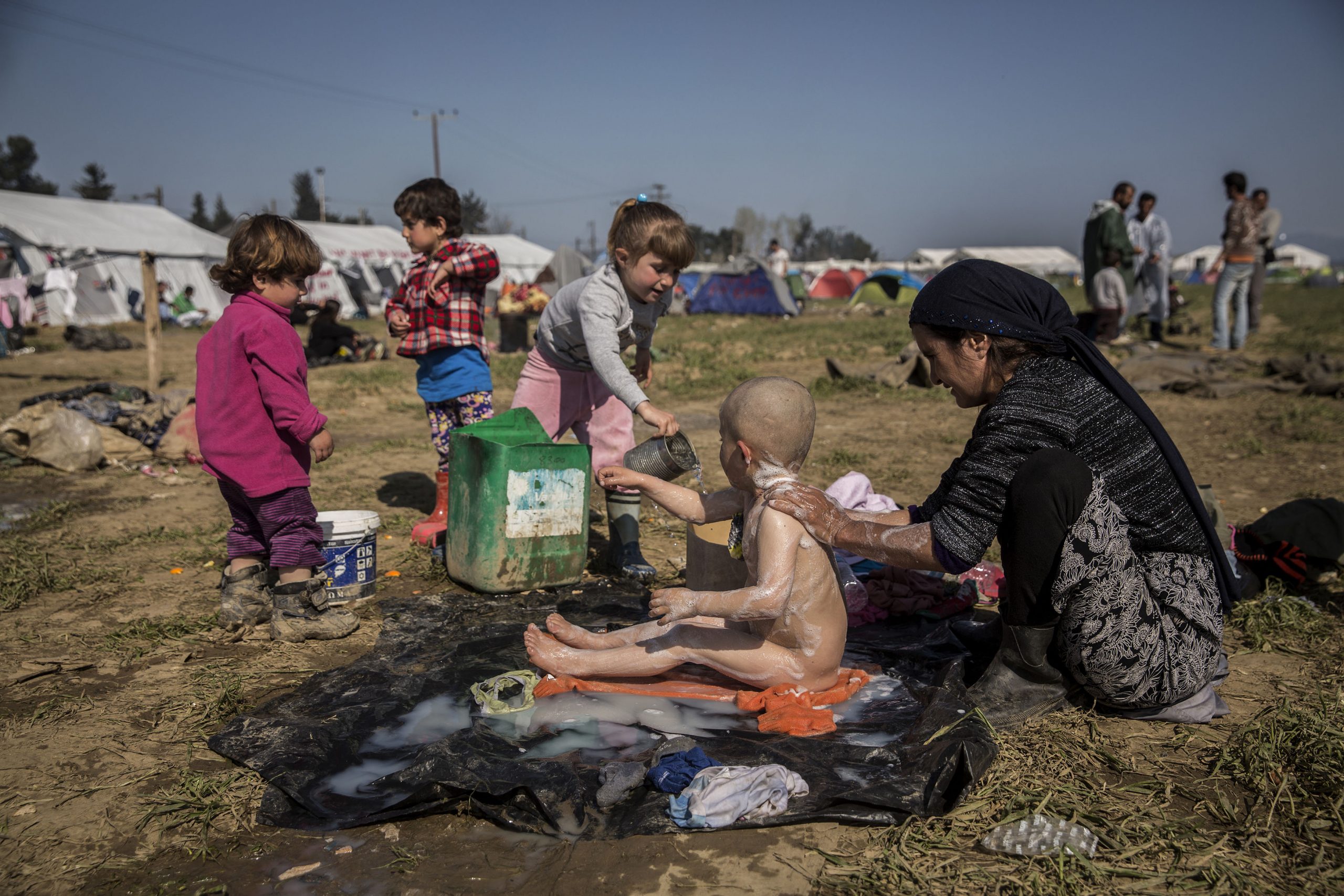 A mother bathes her son in the middle of the camp. The kid was shaved his head because he had lice. Idomeni, 20/03/2016
