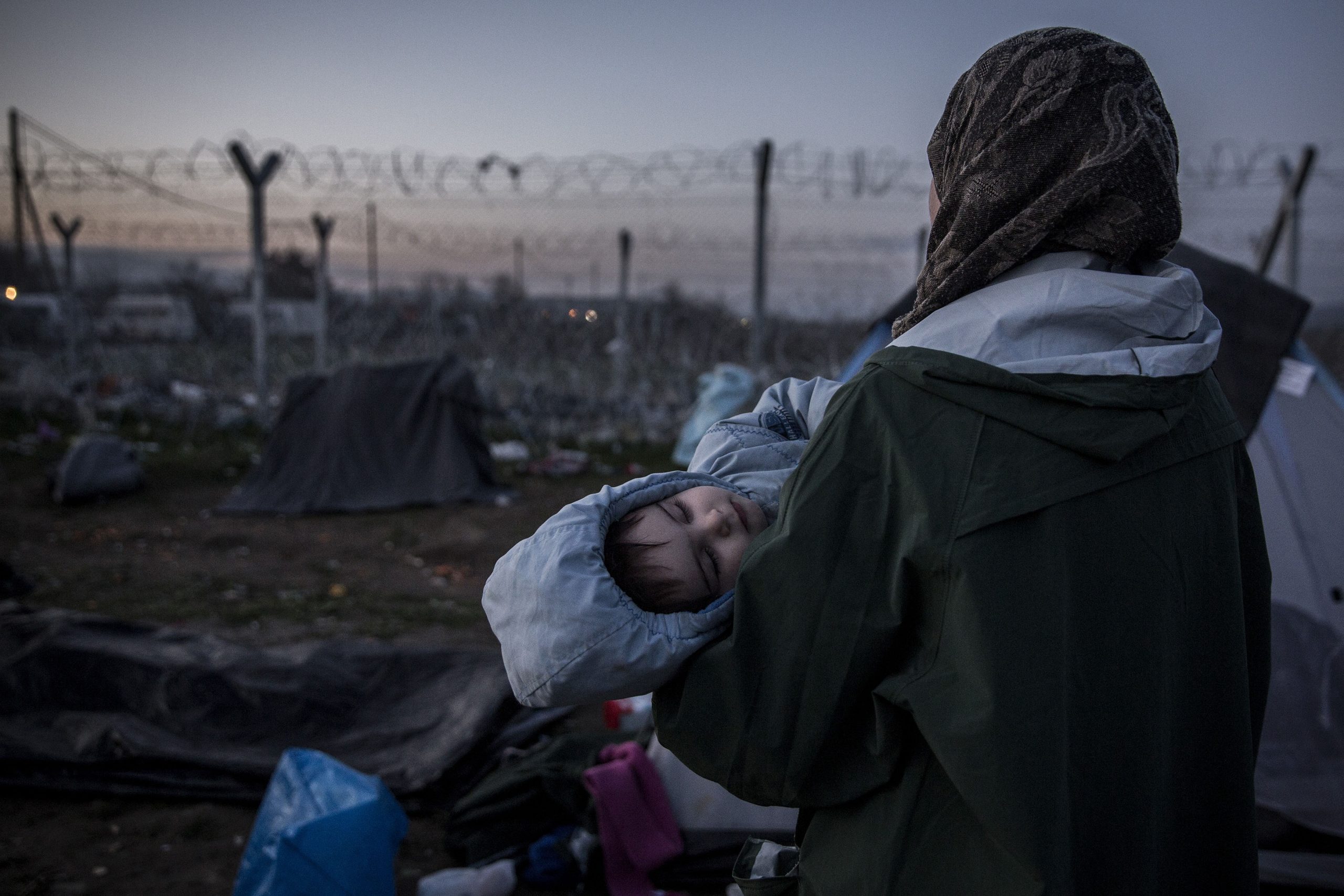 A refugee carry her son in her arms looking at the fence separating Greece and Macedonia. Idomeni, 02/03/2016.
