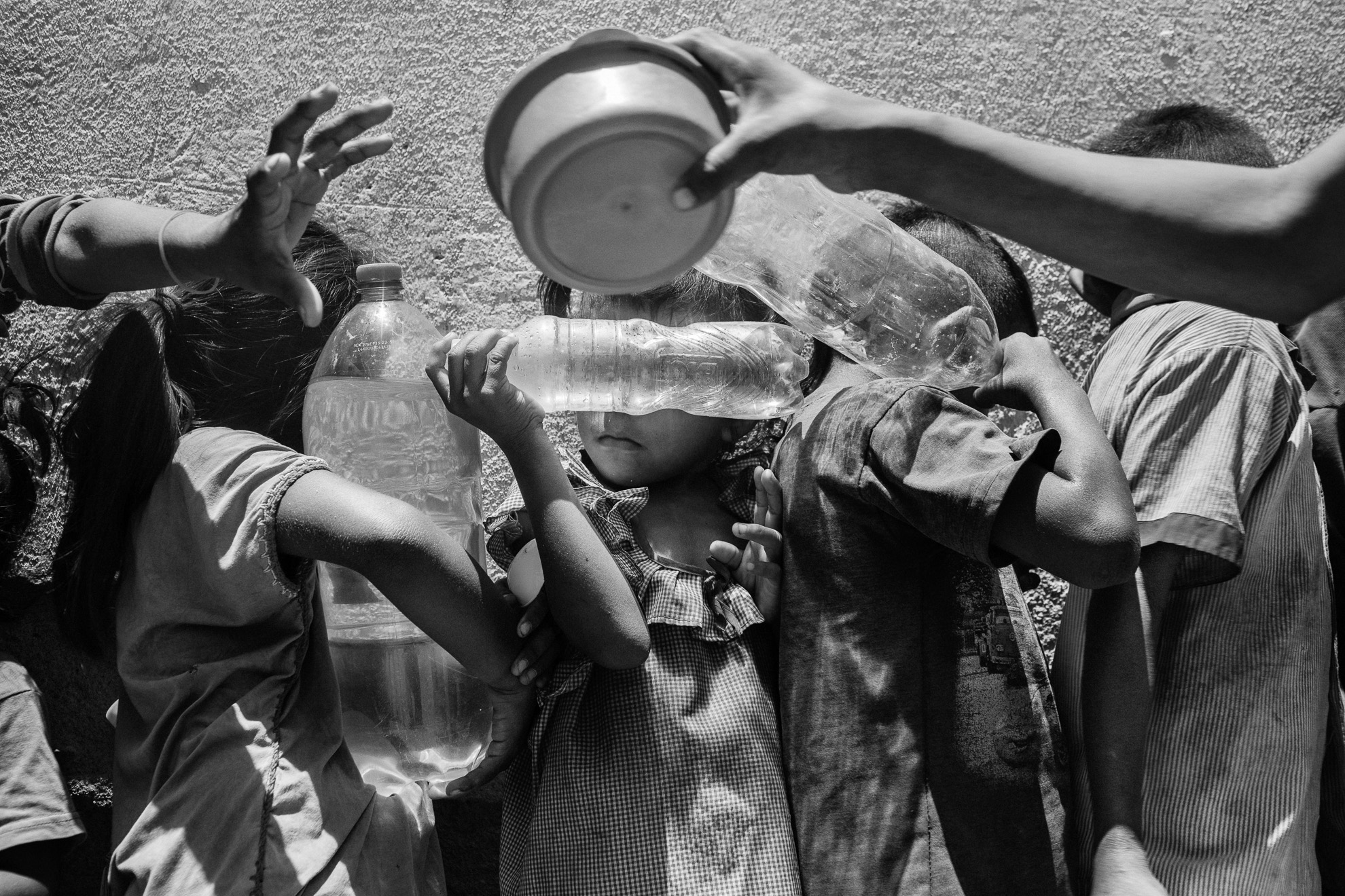 Niños venezolanos que sostienen botellas de plástico para ser llenadas con agua esperan en la fila para una comida gratuita en una organización de caridad en Paraguachón, Colombia.