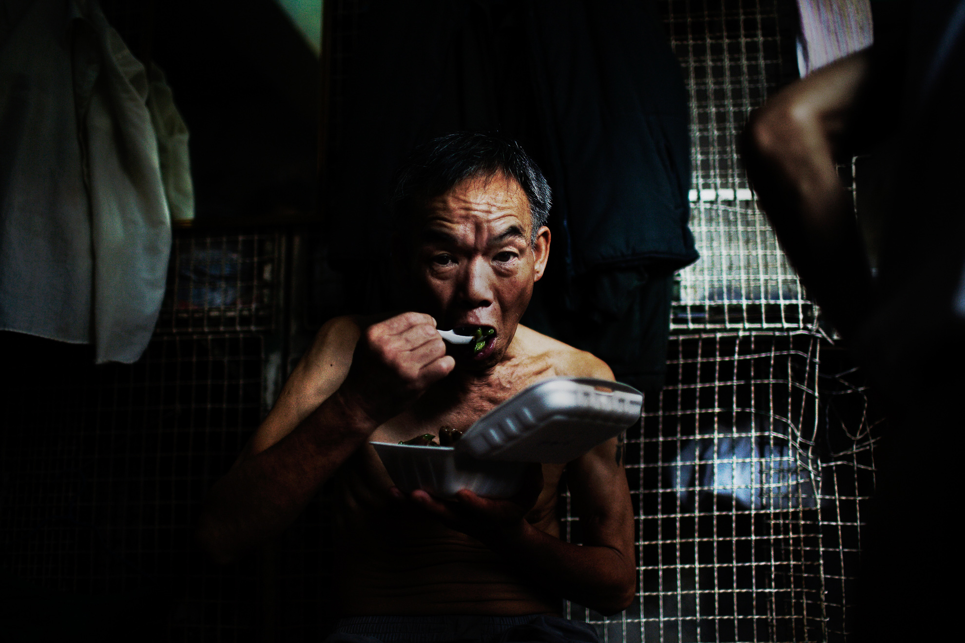 Kong Siu-kau eats in front of his small cage at the Hong Kong's Tai Kok Tsui district, July 16, 2008. In older districts such as Tai Kok Tsui, hundreds of elderly men still reside in caged cubicles in cramped, old tenement flats which house up to 12 individuals in often squalid conditions.
