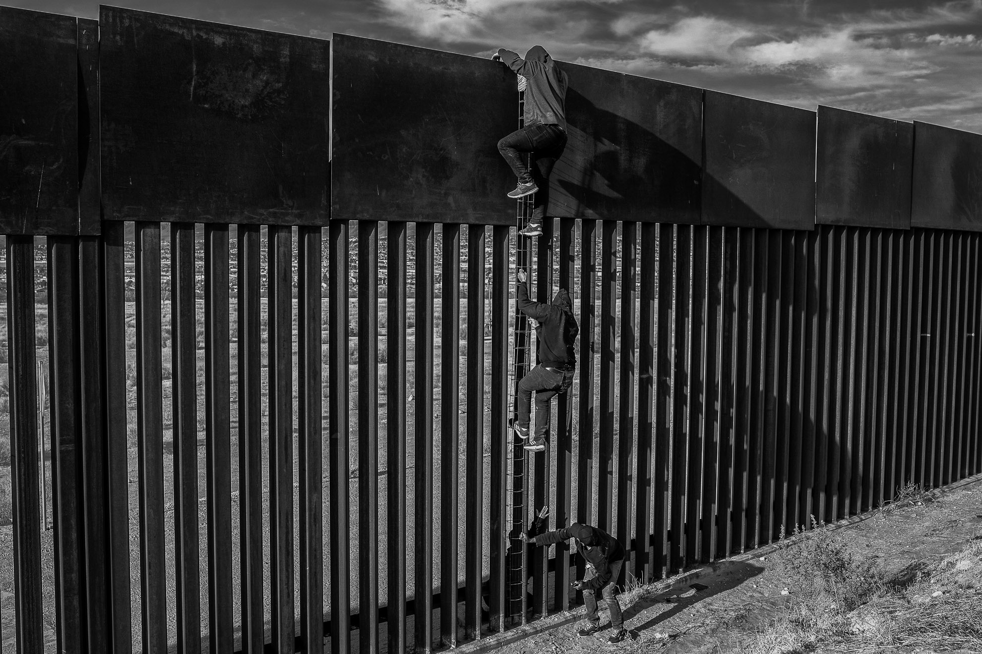 Migrants using and homemade ladder climb the wall in Ciudad Juárez.