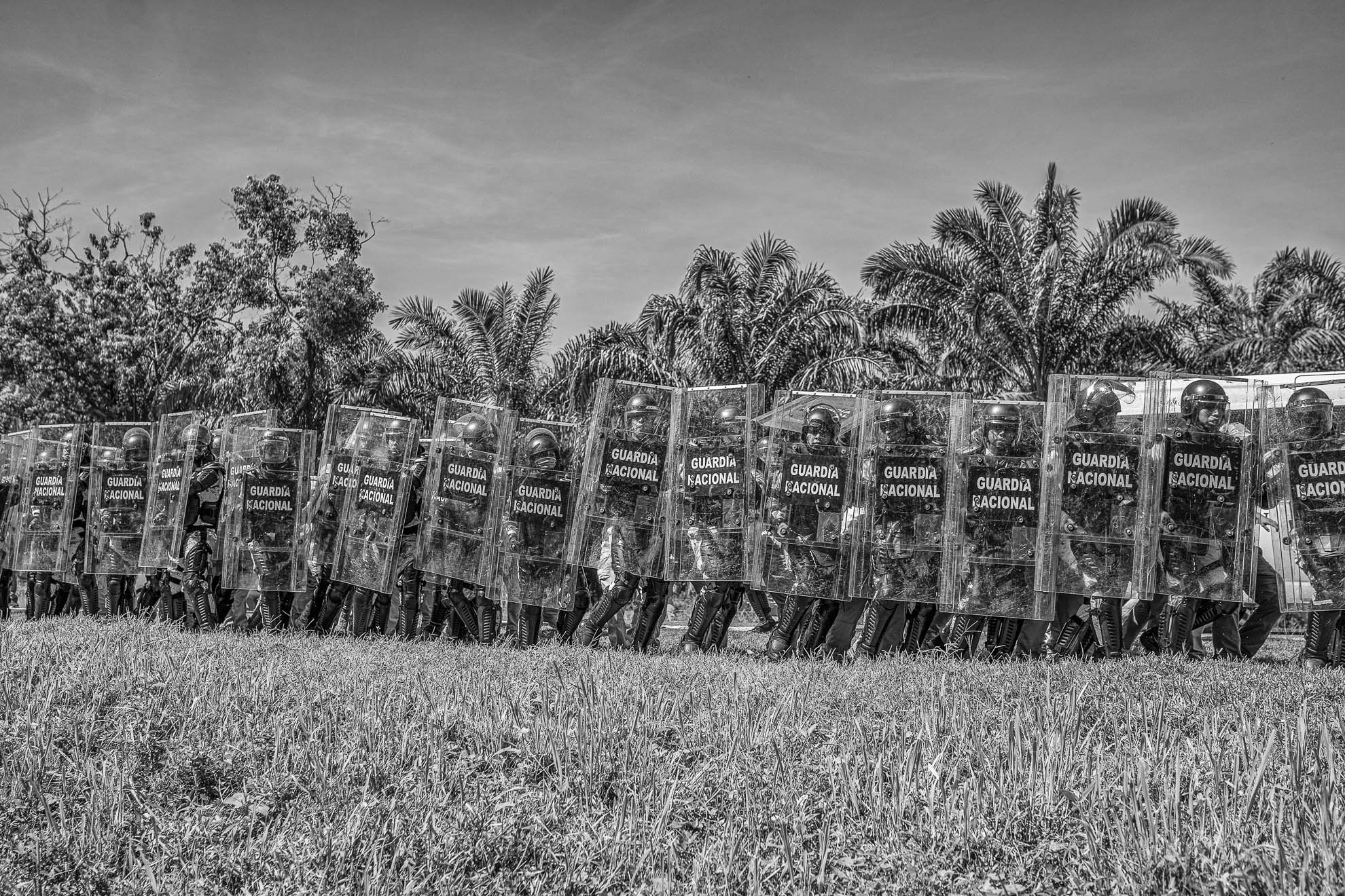 Miembros de la Guardia Nacional en formación de muro de escudo para enfrentar a los migrantes que intentan huir de una redada.
