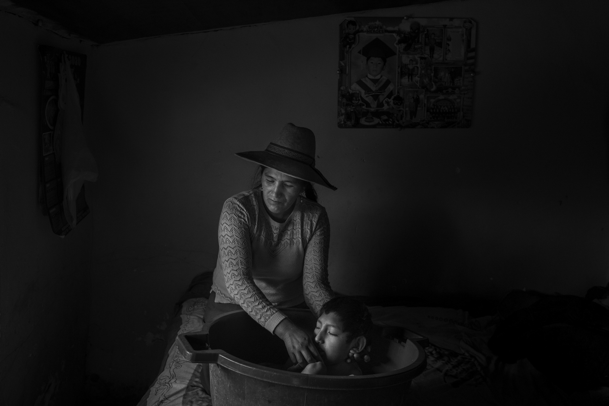 Silvia Chilo Choque, de 40 años, mientras lava a su hijo con parálisis cerebral Julio César Chuahuayo Chilo, de 13 años. Debido a la escasez de agua, muchas personas lavan con agua de lluvia en la época de lluvias. En la estación seca, utilizan agua contaminada del río, hirviéndola primero. Debido a todo este largo proceso, muchas veces la gente puede ducharse una vez a la semana.