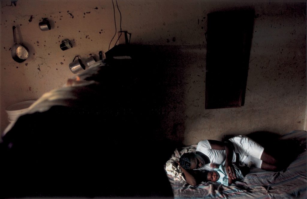 Levia Rodríguez descansa en su cama con su hija recién nacida, Francesca. La casa, de una única sala con una madera que divide la cocina del dormitorio, era un barrancón usado hasta hace poco tiempo para alojar a trabajadores de la caña.