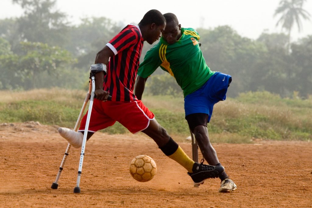 Muchos hombres han perdido un brazo o una pierna como consecuencia de la polio; otros fueron víctimas de accidentes de tráfico (una de las mayores causas de muerte en Ghana). Para muchos de los jugadores, encontrar dinero para el transporte es un desafío semanal constante. Pero la esperanza de convertirse en el primer equipo de discapacitados de Ghana, les mueve a seguir entrenando. Richard Ofei (izquierda) y Richard Opentil compiten por el balón durante la práctica del fútbol en Accra, Ghana. Aunque les falta una pierna, ambos hombres se encuentran entre los jugadores más rápidos del equipo y siguen fácilmente el ritmo de sus compañeros.