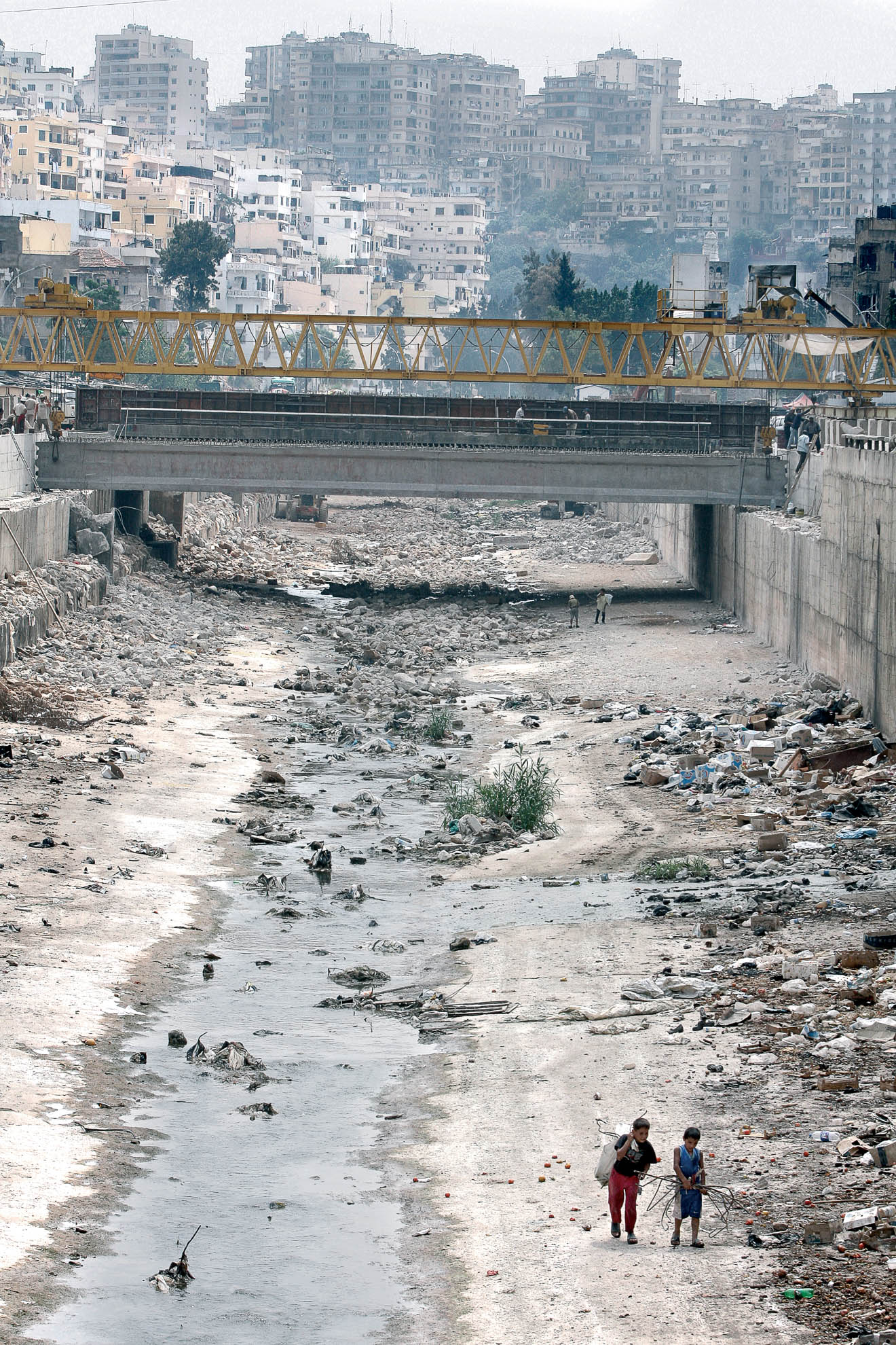 La fotografía muestra un río en la ciudad de Trípoli. Decenas de niños sobreviven recogiendo restos de la basura que arrojan los mercaderes y vecinos de las zonas cercanas al río. Trípoli está al norte del país. Además de la pobreza y las insalubres condiciones de vida, la ciudad es escenario de luchas protagonizadas por las diferentes milicias islámicas, suníes y chiíes, que siembran la ciudad de bombas y protagonizan enfrentamientos armados en sus calles.