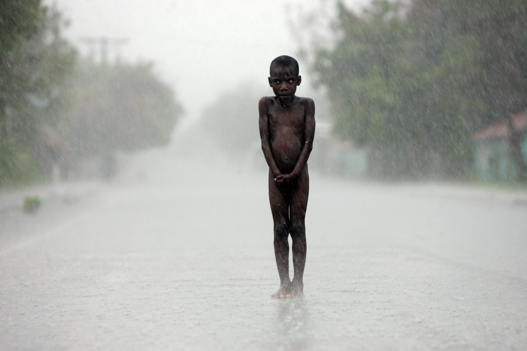 A boy stands in the middle of the road leading to the south of the republic, as intensely heavy rain falls during the passage of Hurricane Dean, just off the Dominican Republic. This photo was taken as I returned to the capital, once the hurricane had moved on to Haitian territory. Visibility was minimal, because of the intense rain fall. After going several kilometers, I saw two naked boys standing in the middle of the road. I motioned to the driver to stop the van, and he pulled up a few meters further on.