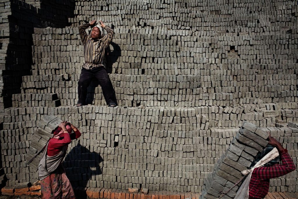 Young workers carrying bricks on their backs.