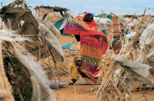 La colorida ropa que viste la mujer contrasta con las condiciones en las que se ha visto forzada a vivir junto a las personas refugiadas del campo de Otash para desplazados internos en el sur de Darfur (Sudán).