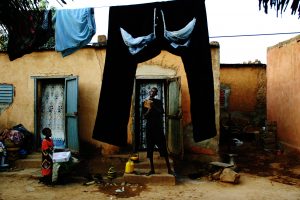 Un hombre se afeita bajo la atenta mirada de la hija de un amigo. Es uno de los ocho compañeros que comparten habitación en la marginal Comuna III de Bamako, Malí, mientras ahorran dinero para emprender el viaje a Europa.