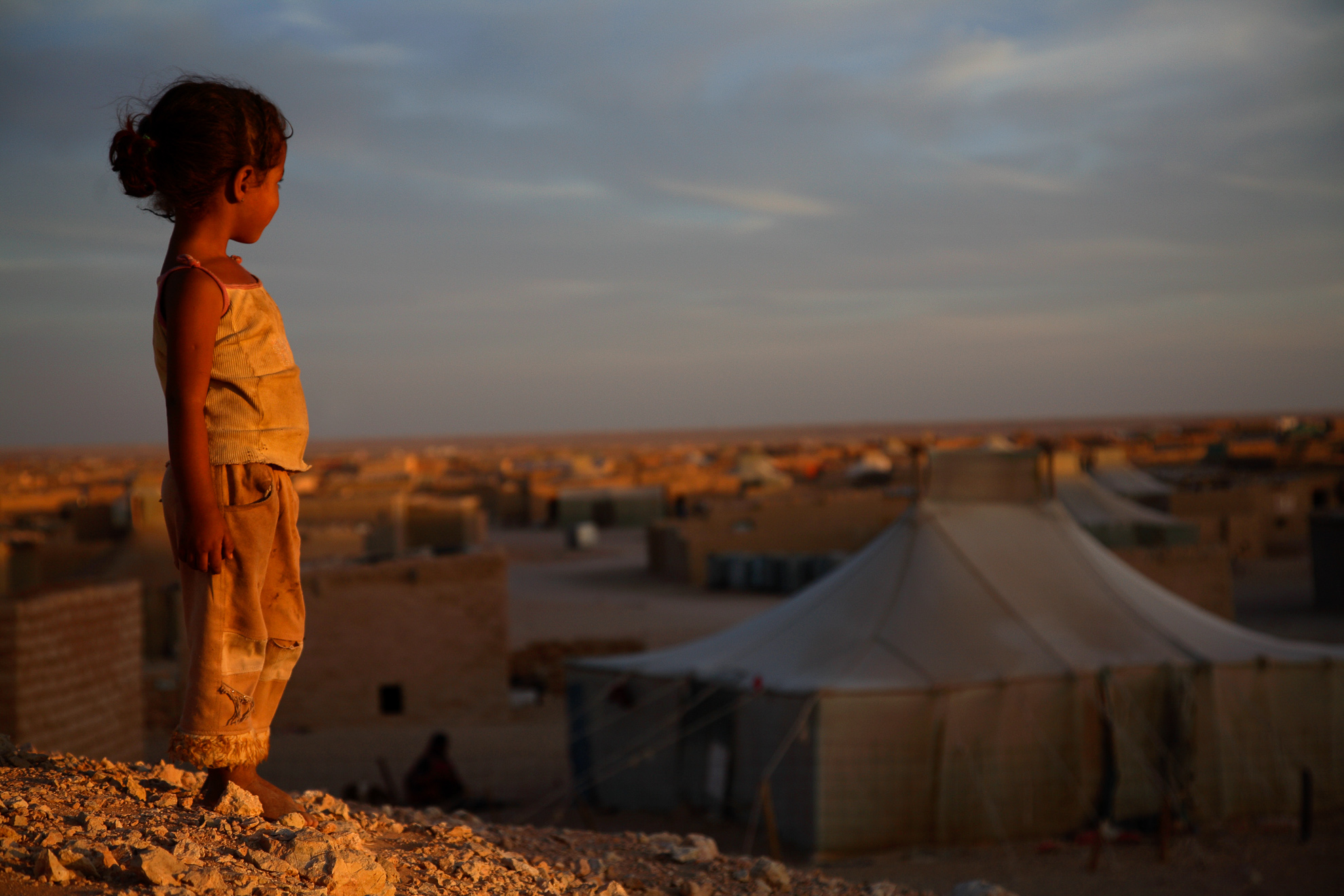 Glana, a four-year-old girl, watches the last rays of sunlight in the Smara refugee camp. In the background, is her family's tent.