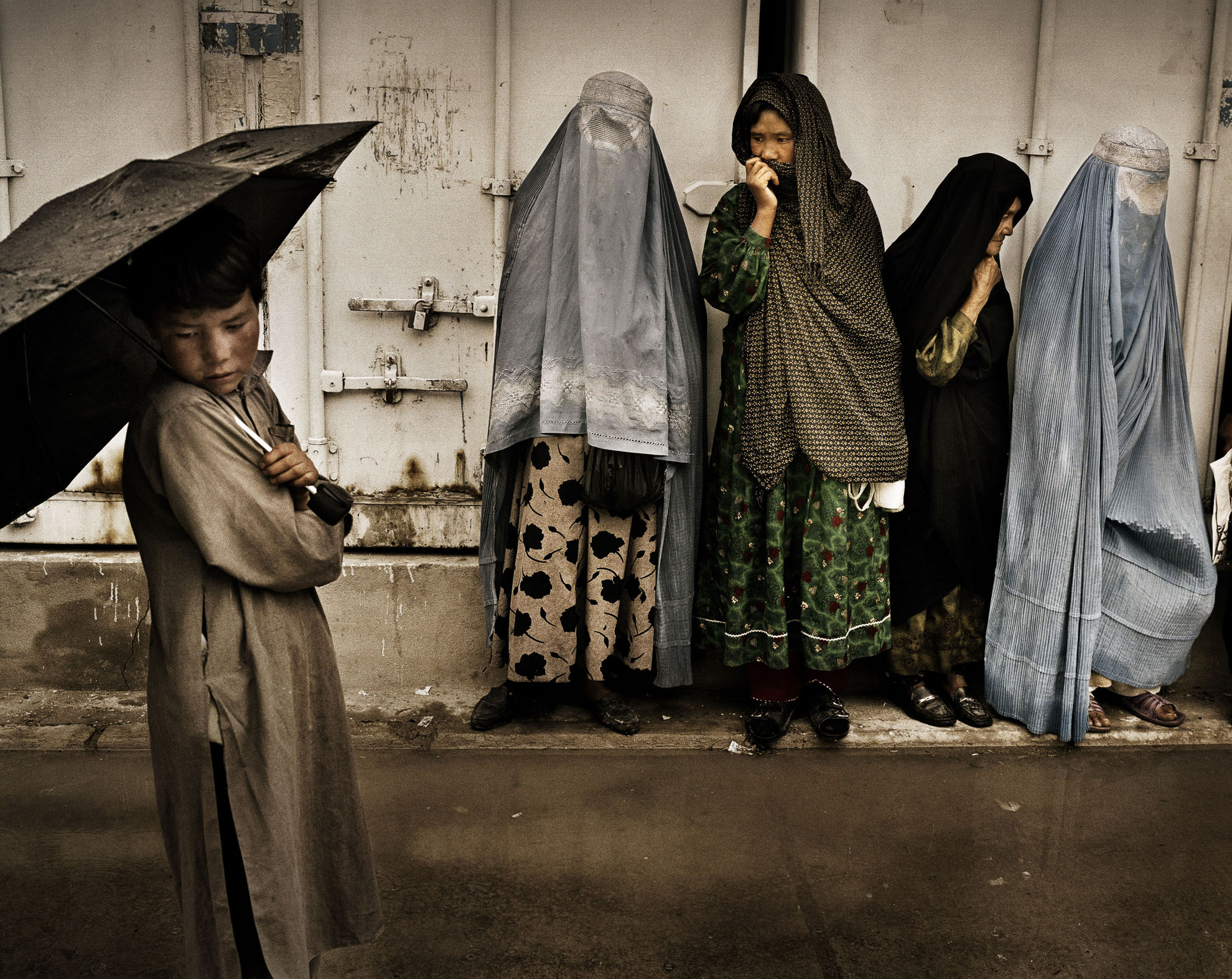 Pacientes del Hospital de Tuberculosis y Enfermedades Contagiosas de Kabul, Afganistán, hacen cola esperando la distribución de comida, en junio de 2007. Un niño de 9 años espera con su madre para ayudarle a llevar la comida de regreso a casa.