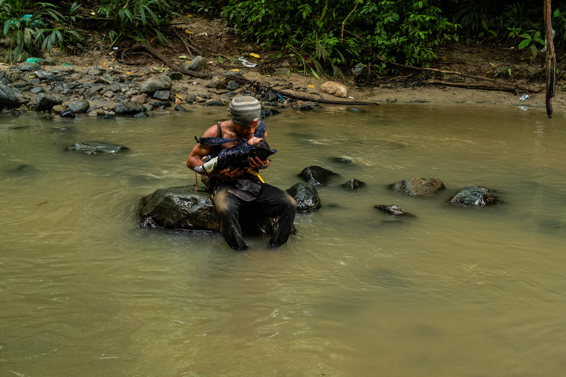 A man kisses his baby, just a few months old, during a break in a creek on the road in the Darien Gap between Colombia and Panama. Forty thousand minors have crossed the jungle so far this year, many of them babies. Like tens of thousands of Venezuelans, they cross this wild and roadless route believing they will reach the United States as their friends and neighbors have done weeks before. September 2022.