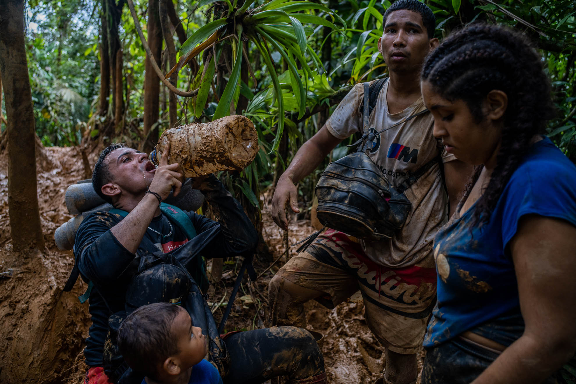 Un hombre toma el último sorbo de agua de un botellón cubierto de lodo. Los migrantes que salen desde Capurganá en Colombia intentan llevar con ellos alimentos y agua para el trayecto. Sin embargo, tras varios días de camino entre la selva y a medida que avanzan en el camino los víveres empiezan a escasear. Octubre de 2022.