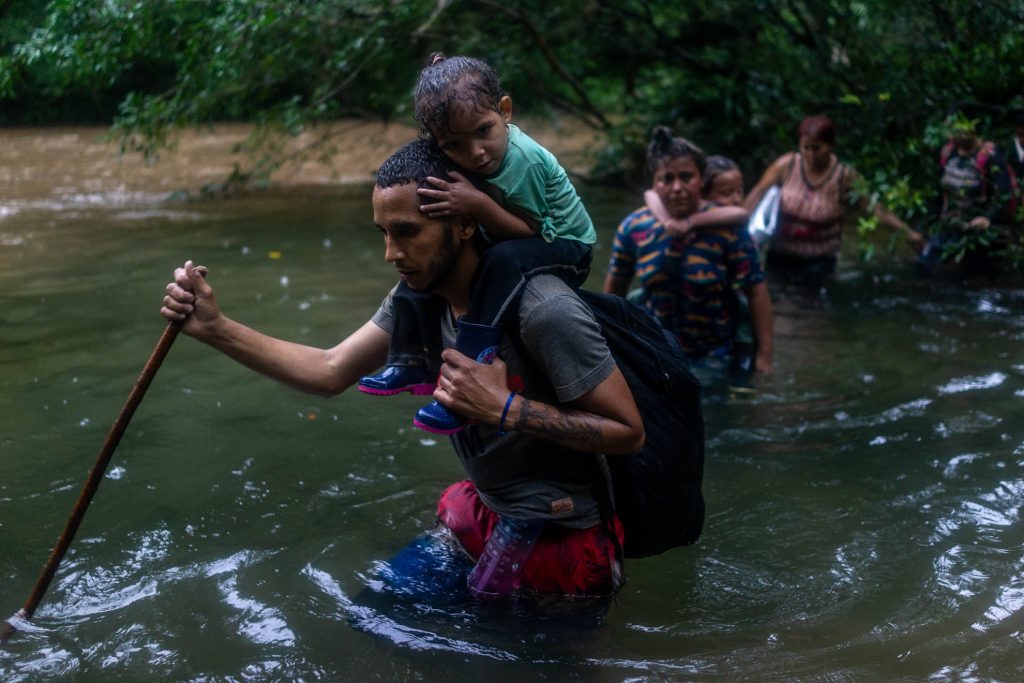 Una familia cruza el río Tacartí con sus hijos en sus espaldas. Varias muertes en la zona se han producido por las crecientes subidas de los ríos que arrastran a las personas y mueren ahogadas. En el Tapón del Darién entre Colombia y Panamá, 2022.