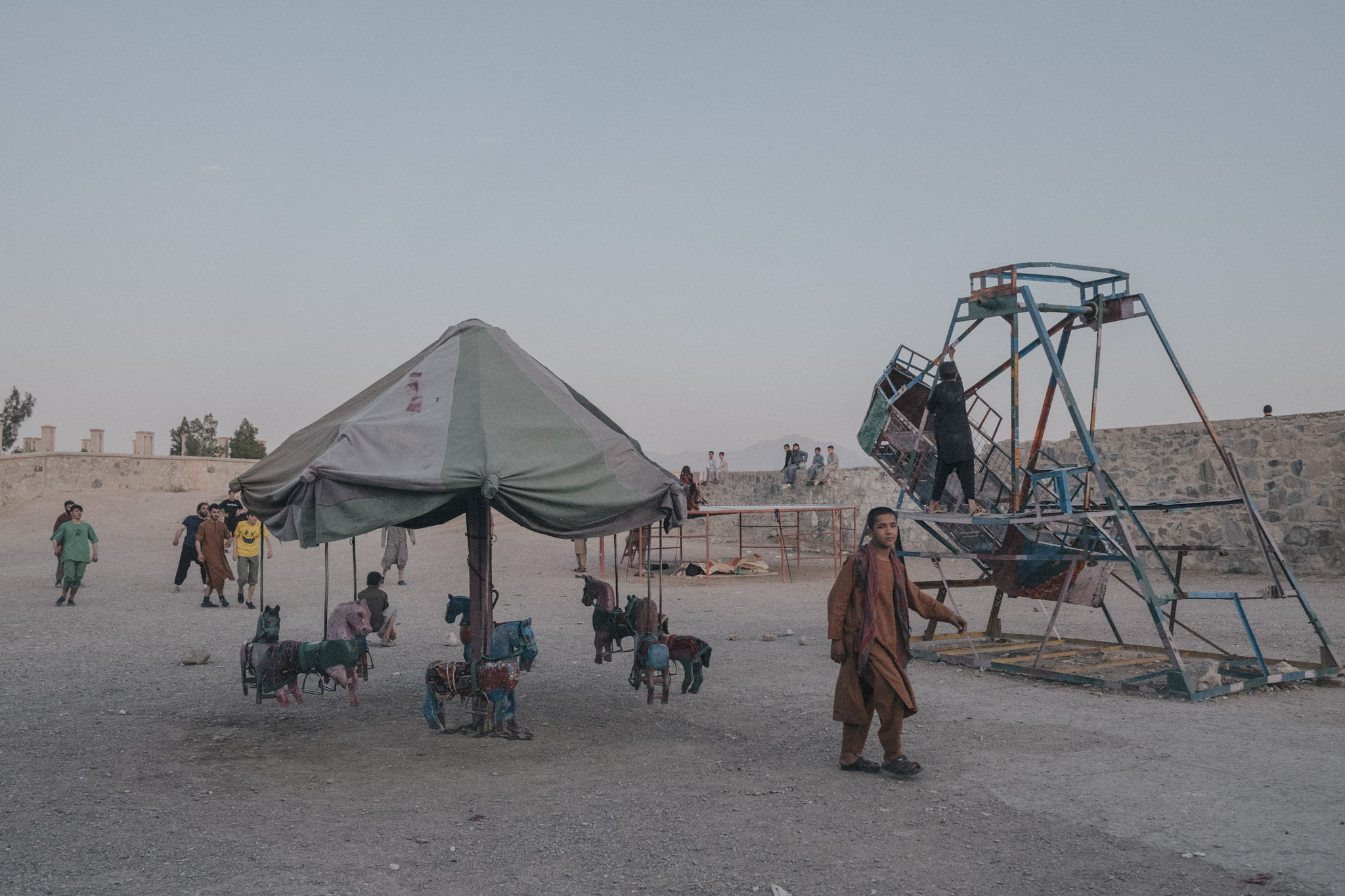 Niños y adolescentes juegan en un pequeño parque de Kabul al atardecer. Desde el regreso de los talibanes, los niños enfrentan hambre severa, explotación y pérdida de oportunidades educativas, especialmente las niñas. Los talibanes han declarado abiertamente que las mujeres deberían evitar salir de sus casas salvo en casos de absoluta necesidad. Las restricciones sobre la vestimenta forman parte de un esfuerzo más amplio por borrar a las mujeres de la vida pública, limitando su movimiento, expresión y participación en la sociedad. Este estricto control sobre los cuerpos y vidas de las mujeres refuerza un sistema patriarcal en el que el hogar es presentado como el único lugar “seguro” para ellas.